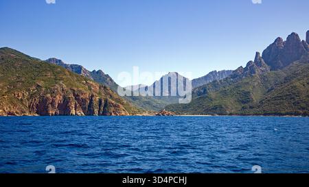 Vista dal mare della piccola città di Porto Ota e della costa con lo sfondo delle montagne al sole e il cielo blu Foto Stock