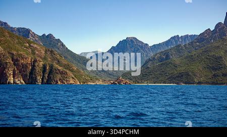 Vista dal mare della piccola città di Porto Ota e della costa con lo sfondo delle montagne al sole e il cielo blu Foto Stock