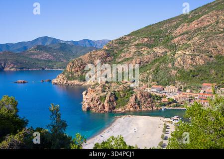Vista dalle montagne della piccola città di Porto Ota, la torre genovese sulla roccia rossa e la spiaggia al sole e al cielo azzurro Foto Stock