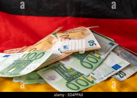Baviera, Germania - 10 novembre 2025: Un mucchio di banconote in euro davanti alla bandiera tedesca un'immagine simbolica del debito nazionale, del bilancio federale e delle sfide di politica fiscale della Germania per affrontare disavanzi e spese. *** Ein Stapel Euro-Banknoten vor der deutschen Flagge Symbolbild für Staatsschulden, Bundeshaushalt und finanzpolitische Herausforderungen Deutschlands im Umgang mit Defiziten und Ausgaben Foto Stock