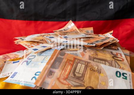 Baviera, Germania - 10 novembre 2025: Una pila di banconote in euro davanti alla bandiera tedesca, simbolo della situazione economica, dell'inflazione, dell'attività economica e dello sviluppo finanziario in Germania. *** Ein Stapel Euro-Banknoten vor der deutschen Flagge Symbol für Wirtschaftslage, Inflation, Konjunktur und finanzielle Entwicklung in Deutschland. Foto Stock
