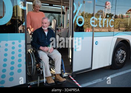 Coppia senior che utilizza un autobus pubblico elettrico accessibile con sedia a rotelle Foto Stock