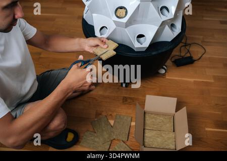 Vista ad angolo alto del giardinaggio maschio che taglia lana di roccia con forbici, preparazione di terreni idroponici per l'avviamento dei semi, evidenziando la precisione in ambienti interni Foto Stock