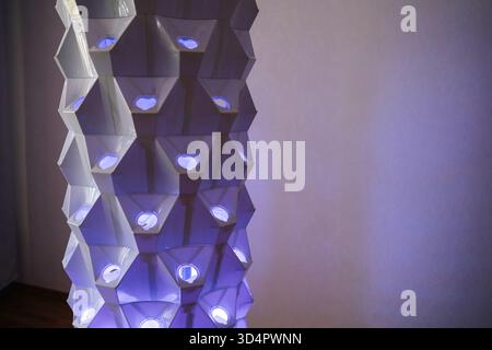 Torre idroponica verticale con luci blu che illuminano la struttura geometrica che mette in risalto l'innovativa tecnologia agricola per interni Foto Stock
