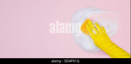 Il guanto giallo contiene spugna e salviette in schiuma di sapone su sfondo rosa Foto Stock
