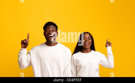 Happy Young coppia che festeggia con Big Smiles e Raised Fingers su sfondo giallo brillante Foto Stock