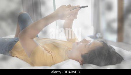 Uomo asiatico che giace, indossa una maglietta gialla e un jeans blu, tenendo un tablet sopra il viso in camera da letto Foto Stock