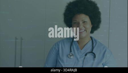 Infermiera sorridente che posa il torace in clinica, indossa scrub azzurro, stetoscopio Foto Stock
