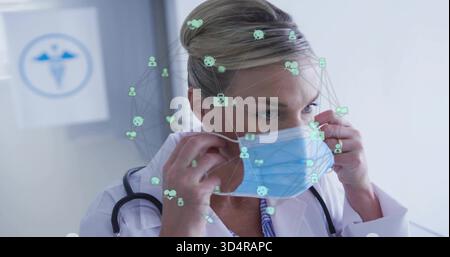 Medico adattivo nel camice da laboratorio per fissare la maschera azzurra in clinica, stetoscopio, icone digitali Foto Stock