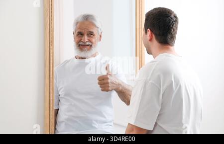 Il giovane si vede come un anziano allo specchio. Concetto di personalità, passato e futuro, flusso del tempo, età Foto Stock