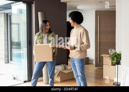 Utilizzo di scanner palmare, operaio delle consegne e donna indiana che sposta scatole di cartone in soggiorno Foto Stock