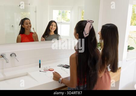 Diverse amiche che chiacchierano e si truccano sul lavandino del bagno, con spazzole e tavolozza Foto Stock