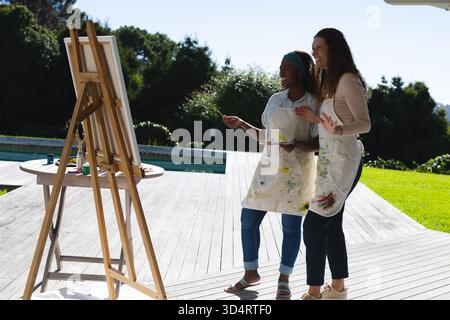Diverse amiche che lavorano su tela sul ponte a bordo piscina, con cavalletto, tavolozza, spazio per copiare Foto Stock