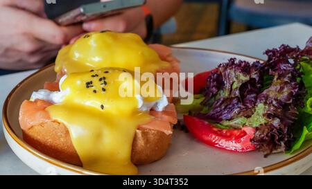 Gustose uova benedict con salmone affumicato e ricca salsa hollandaise su un piatto accompagnato da un'insalata vivace, ideale per un pasto delizioso Foto Stock