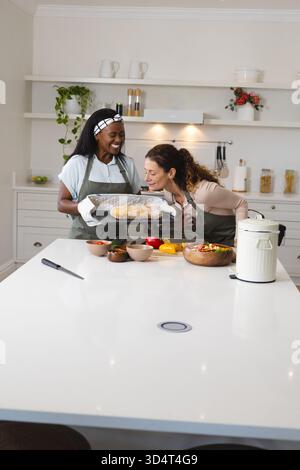 Ispezionare il pane appena sfornato diverse amiche che si trovano a Kitchen Island, con vassoio da forno Foto Stock