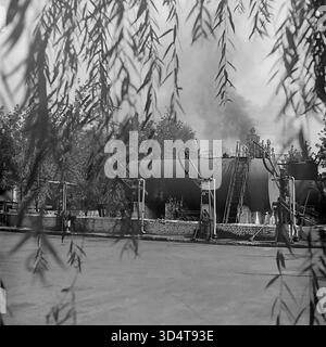 Una suggestiva foto in bianco e nero degli anni '1970 mostra il deposito petrolifero di Sloviansk, la RSS Ucraina. La scena è incorniciata artisticamente da foglie di salice appese. Al centro, sono visibili un grande serbatoio di stoccaggio orizzontale e le pompe del carburante. Sullo sfondo, un'alta ciminiera industriale fuma attivamente, segnalando un impianto di lavoro. Questo cattura il pesante paesaggio industriale e l'atmosfera di lavoro del pacifico Donbas in epoca sovietica. Foto Stock