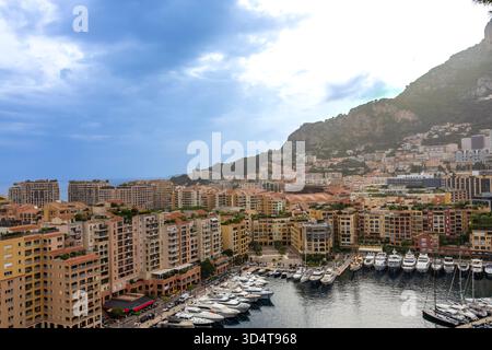 28.08.2025 FR. Monaco. Edifici a più piani circondano il porto pieni di yacht di lusso, adagiati sullo sfondo di un'alta collina rocciosa. Foto Stock