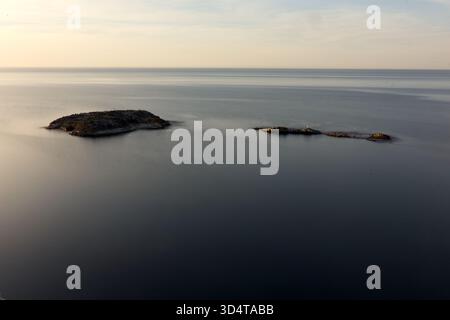 La delicata luce autunnale illumina una vasta distesa di oceano calmo, con un lungo molo che si estende sull'orizzonte sotto i cieli pastello Foto Stock