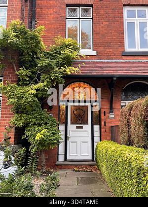 Un'affascinante casa in mattoni rossi in stile vittoriano ricoperta di edera verde, caratterizzata da una porta in vetro colorato splendidamente realizzata. Catturato a Hull, nell'East Yorkshire Foto Stock