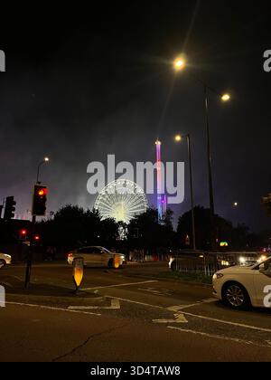 Una vista notturna della strada a Hull caratterizzata da luminosi semafori, traffico di passaggio e una ruota panoramica illuminata che si illumina in lontananza. Fumo e bugia Foto Stock