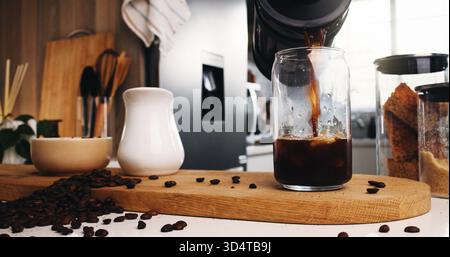 Caffè ghiacciato, vetro e liquido in cucina per una forte caffeina, versare o arrostire in casa. Birra biologica, bevande e fagioli con French press per mocha Foto Stock