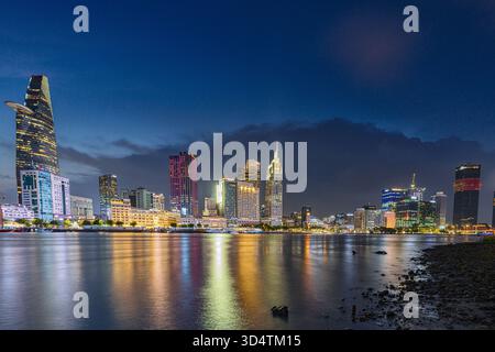 La vista di un vivace paesaggio urbano si illumina con luci colorate che si riflettono sul tranquillo fiume sotto un cielo crepuscolo, ho chi Minh City, ho chi Minh City, Vietnam. Foto Stock
