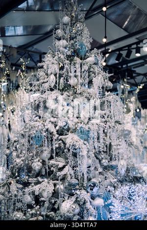 Albero di Natale smerigliato decorato con ornamenti argentati, bianchi e blu, ghiaccioli e luci in uno spazio commerciale. Elegante tema per le vacanze. Varsavia, Polonia Foto Stock