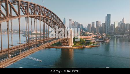 Vista ravvicinata dell'arco del Sydney Harbor Bridge sul porto di Sydney, che collega la riva nord al vivace quartiere centrale degli affari, piccola barca che naviga nelle acque. Architettura e trasporti. Panorama aereo Foto Stock