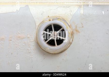 Primo piano di un vecchio scarico della vasca da bagno colorato con smalto bianco sbucciato e sporcizia visibile, che mostra texture e segni di usura per la manutenzione o la pulizia Foto Stock