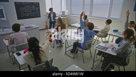Durante la lezione sullo sviluppo del gioco, l'insegnante spiega l'argomento e pone domande. Gli studenti alzano la mano, pronto risposta. Concetto di istruzione moderna, apprendimento interattivo e istruzione STEM. Colpo statico. Foto Stock