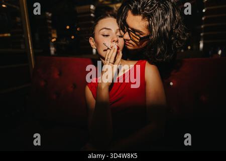 Serata intima con gli amici: La donna in abito rosso fuma mentre l'amica si appoggia Foto Stock