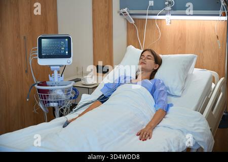 Donna che riceve terapia endovenosa mentre riposa nel letto d'ospedale Foto Stock