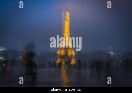 Parigi, Francia - 2 novembre 2025: Veduta della Torre Eiffel illuminata che attraversa il crepuscolo, il suo bagliore dorato riflesso nel terreno bagnato, sur Foto Stock