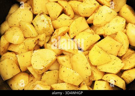 Vista ravvicinata a tutto campo delle patate gialle crude a dadini condite con pepe nero e olio all'interno di una pentola nera. Foto di alta qualità Foto Stock