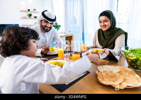 Famiglia del Medio Oriente che indossa abiti tradizionali degli emirati trascorrendo del tempo insieme a casa. Famiglia del Medio Oriente con bambini seduti a un tavolo da pranzo Foto Stock