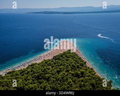 Vista aerea di Zlatni Rat, una spiaggia di corni dorati che si estende nell'azzurro Mare Adriatico, brulicante di bagnanti e incorniciata da una vibrante foresta verde, Bra Foto Stock