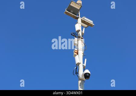 Telecamera di sorveglianza e apparecchiature di sicurezza montate su un'asta metallica alta contro un cielo azzurro, utilizzate per il monitoraggio e la pubblica sicurezza Foto Stock
