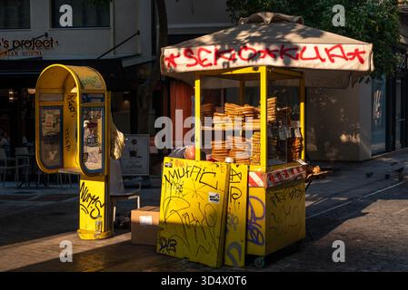 Il 24 agosto 2023, ad Atene, in Grecia, il venditore ambulante vende anelli di pane con cabina telefonica coperta da graffiti Foto Stock