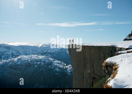 Due escursionisti in piedi su una scogliera innevata con montagne sullo sfondo. Preikestolen, Lysefjord in Norvegia Foto Stock