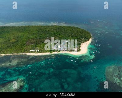 Villaggio costiero con case raggruppate circondato da foresta tropicale e barche ancorate vicino alla spiaggia. Isola di Daku. Siargao, Filippine. Foto Stock