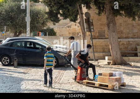 gerusalemme, Israele, 2 novembre 2025, Una scena di strada in cui un uomo sta usando un camion per spostare le scatole su un pallet di legno, con un altro uomo seduto sul Foto Stock