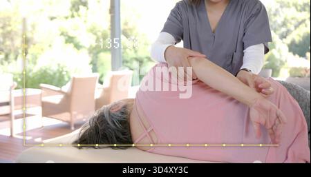 Aiutare il terapeuta in scrub grigi a guidare il paziente con la parte superiore rosa sul tavolo imbottito vicino alle finestre, sovrapposizione Foto Stock
