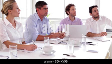 Quattro colleghi seduti in un abbigliamento casual per affari discutono di progetti nella sala meeting, con un computer portatile Foto Stock