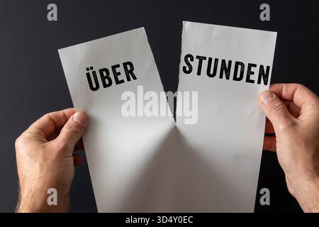 Baviera, Germania - 10 novembre 2025: FOTO DI MONTAGGIO, due mani con un foglio di carta strappato con la parola "straordinari". Immagine simbolica del diritto del lavoro, riduzione e confisca degli straordinari per i dipendenti *** FOTOMONTAGE, Zwei Hände halten ein zerrissenes Blatt Papier mit dem Wort Überstunden. Symbolbild Arbeitsrecht, Abbau und Verfall von Überstunden bei Arbeitnehmern Foto Stock