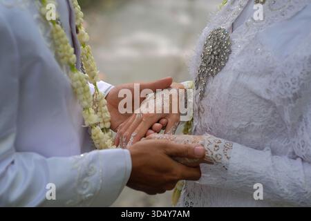 Primo piano di una coppia di sposi che si tengono a vicenda con amore. Entrambi erano vestiti con abiti da sposa tradizionali bianchi. Foto Stock
