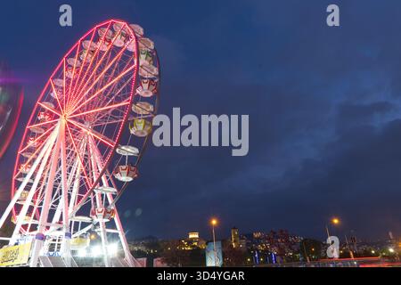 Una scena notturna drammatica caratterizzata da una ruota panoramica illuminata, prevalentemente di rosso vivo. L'aspetto statico della ruota (o molto lento Foto Stock