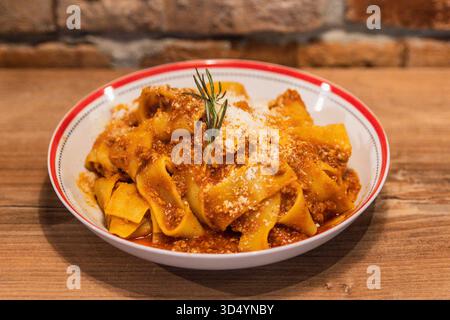 Delizioso piatto di pappardelle bolognesi condito con ricco sugo di carne e guarnito con rosmarino e parmigiano grattugiato Foto Stock