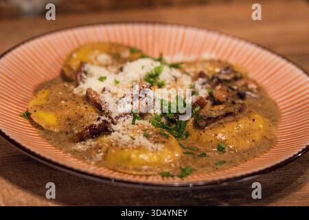 Ravioli fatti in casa con funghi porcini e guanciale croccante, serviti in salsa cremosa e guarniti con prezzemolo e parmigiano Foto Stock