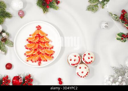 Piatti di Natale e Capodanno. Albero di Natale commestibile fatto di mandarini e melograno per una tavola festosa, un'idea per decorare cibo e decorazioni Foto Stock