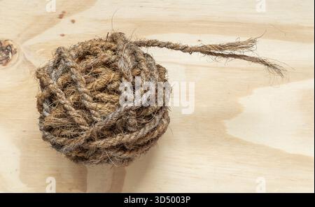 Una palla di spago marrone rustico e grossolano o una corda in fibra naturale si appoggia su compensato chiaro. Foto Stock